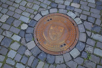 Round rusty manhole cover with city coat of arms and inscription university town, year, round,