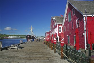 Harbour with red buildings and a boat on the water along a wooden jetty under a blue sky, fishing,