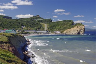 Coastal landscape with hills, cliffs and houses, the sea and waves under a clear blue sky, Perce,