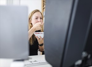 Food at work: A woman eats muesli with fruit in the office. Berlin, 25.07.2024