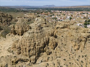 Imposing rock formations in front of a wide, bare landscape with a small village in the distance,