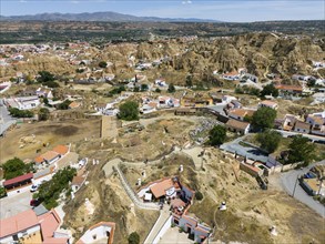 Aerial view of a village surrounded by hilly and stony landscape with mountains in the background,