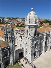 Large Gothic cathedral with high towers and a dome, surrounded by a cityscape under a blue sky,