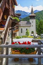 Old wooden house with floral decorations, Saint Theodule church in the background, historic village