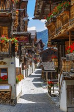 Paved footpath surrounded by old wooden houses, flower boxes on balconies and windows, historic