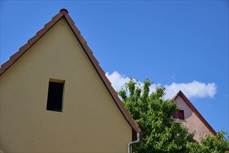 Two houses with gabled roofs, one beige and one pink, in front of a blue sky with scattered clouds