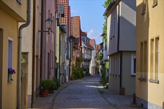 Idyllic narrow alley with cobblestones and traditional houses decorated with flowers under a bright