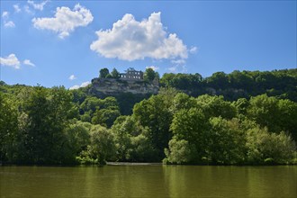 Ruin Karlburg on a hill above the river Main, surrounded by lush green trees under a blue sky with