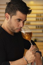 A young Latino man enjoys craft beer in a pub, concentrating on the aroma of the lager he is