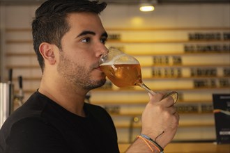 Close-up of a young Latino enjoying a glass of beer in a pub. His satisfied expression and relaxed