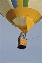 A colorful hot air balloon with a woven basket is soaring in a clear sky, Montgolfière in Charente