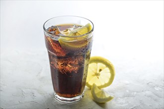 Fresh cola with ice cubes and lemon slices in a drinking glass, sweet caffeine drink against a