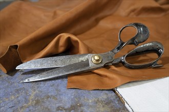 Big old scissors lying on a piece of leather in a craft workshop, copy space, selected focus,