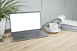 Mock up on an open laptop with a blank white screen, coffee cup and ring binder on a wooden office