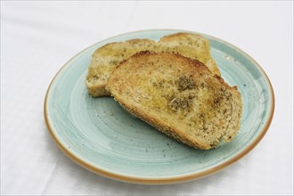 Toasted bread with olive oil, herbs and garlic salt on a blue plate, copy space, selected focus,