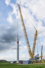 Giant crane is moving a tower part from steel of a wind turbine onto the first tube, heavy industry