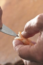 Hand holding a shrimp and removes the guts with a knife, preparation for cooking a seafood meal,