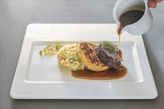 Pouring sauce on a dish from roast venison, flat bread dumpling and round shaped cabbage vegetable