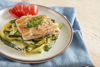 Salmon fillet with parsley garnish, zucchini vegetables and tomato on a light plate, blue napkin