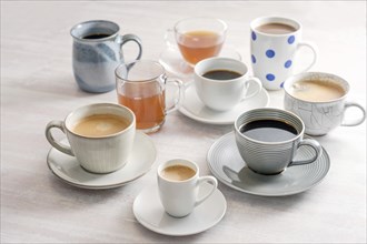 Group of different cups and mugs with coffee and tea drinks on a light table, selected focus,