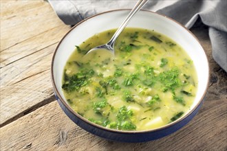 Potato parsley soup in a plate with spoon on a rustic wooden table, healthy vegetarian dish, copy