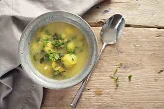 Vegetable soup with brussels sprout, leek and potato in a bowl, spoon and napkin on a rustic wooden