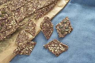 Crunchy whole grain snacks from oat and linseed topped with various seeds on baking paper and a