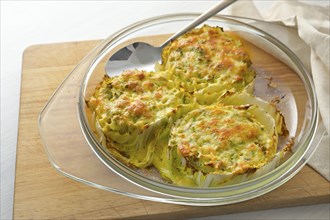 Baked slices of Chinese or napa cabbage in a glass casserole on a wooden kitchen board, creative