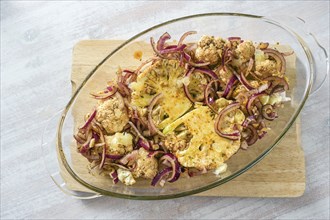 Baked cauliflower steaks with spicy oil and red onions in a glass casserole on a wooden kitchen