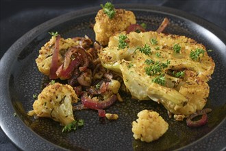 Baked spicy cauliflower slices with red onions on a black plate, healthy vegetable dish for low