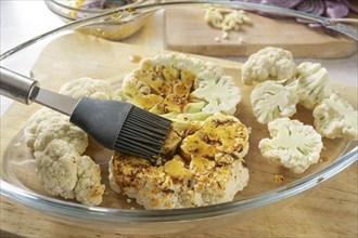 Raw cauliflower slices in a glass casserole are coated with a mixture of spices, herbs and olive