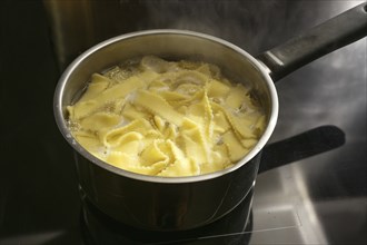 Pasta noodles are cooked in boiling water in a pot on a black stove top, preparing food concept,