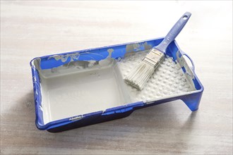 Blue paint tray with light gray lacquer and a brush on a wooden table, craft concept for