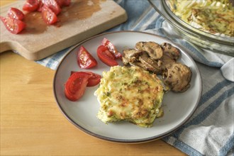 Gratinated Chinese cabbage with mushrooms and tomatoes, healthy vegetarian dish on a wooden table,