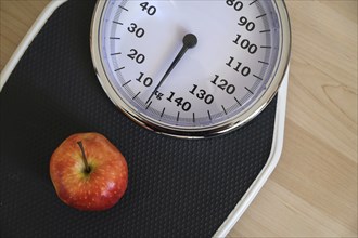 Red apple on an analogue personal scale on a wooden floor, concept for healthy eating, lose weight