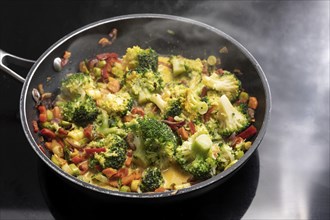 Vegetarian curry with broccoli and other vegetables in a steaming frying pan on a black stovetop,