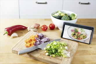 Cut vegetables on a wooden kitchen board, picture of the finished recipe on the smartphone, cooking