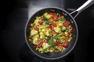 Stir-fried vegetable meal from broccoli, bell pepper, onion and tomato in a frying pan on the black