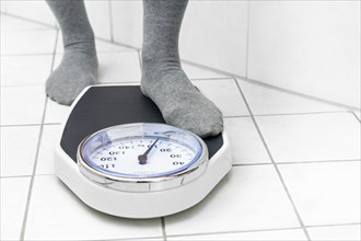 Feet in socks stepping on a personal scale on the tiled bathroom floor to measure the body weight,