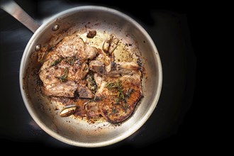 Roasted pork chops with herbs, spices and garlic in a frying pan on a black cooktop, food and