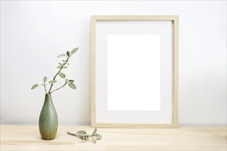 Empty wooden picture frame with passe-partout as mock-up and a vase with sage twig on a light table