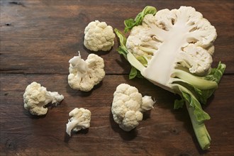 Halved raw cauliflower and some pieces on a dark rustic wooden table, healthy food concept, copy