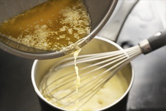 Cooking process of hollandaise sauce, pouring melted butter into the pot with egg mixture, whisking