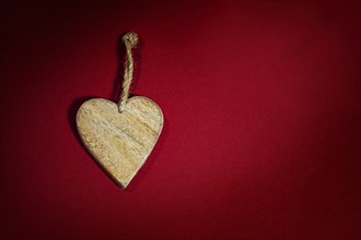 Simple heart shape made of wood with a rustic cord on a background of dark red felt, holiday