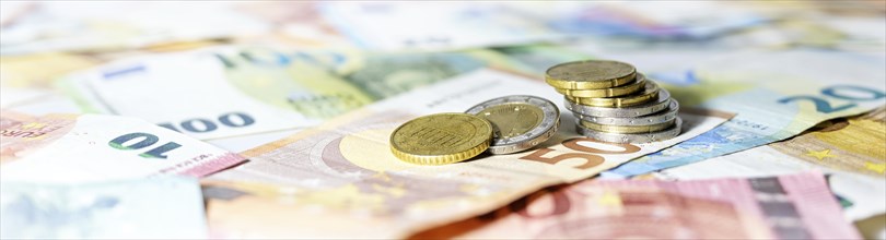 Stack of coins on euro banknotes as wide panoramic format, website header concept for business,