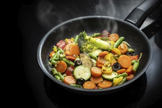 Stir fry vegetables in a black pan with carrots, zucchini, broccoli, green beans, olives and herbs,