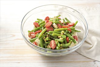 Green bean salad with tomatoes, pine nuts and feta cheese in a glass bowl on a light wooden table,