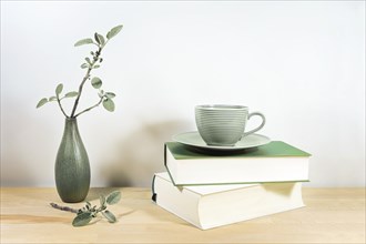 Wooden desk or table with books, a green tea cup and sage twigs in a small ceramic vase against a