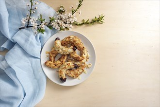 Almond crescent cookies on a plate, spring flower branch and blue napkin on a light wooden table,