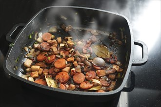 Roasted vegetables for a tasty sauce base in a black cooking pan with carrots, onions, leeks,